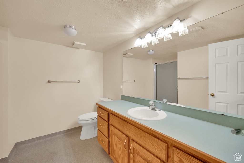 Full bath with an enclosed shower, vanity, toilet, and a textured ceiling