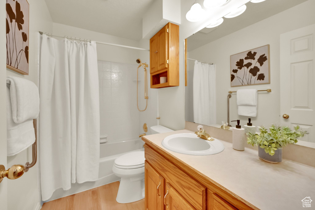Bathroom with toilet, wood finished floors, shower / tub combo with curtain, and vanity