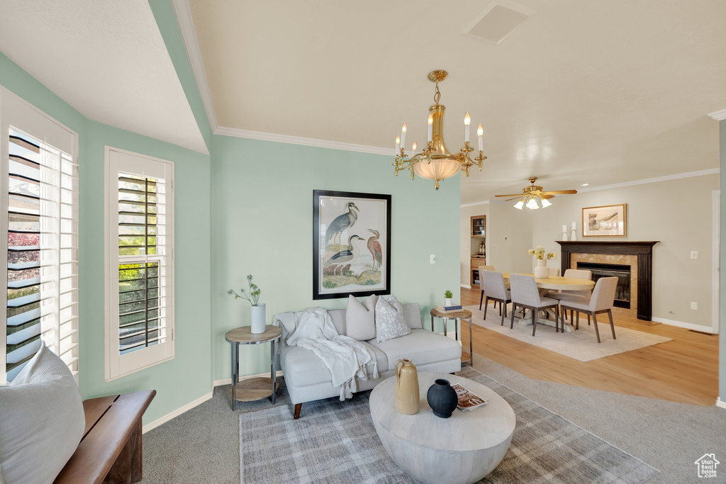 Carpeted living area featuring wood finished floors, baseboards, ceiling fan with notable chandelier, a glass covered fireplace, and ornamental molding