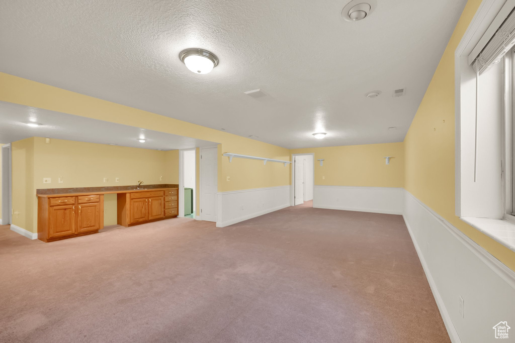 Finished basement with light colored carpet, a sink, a textured ceiling, and indoor wet bar