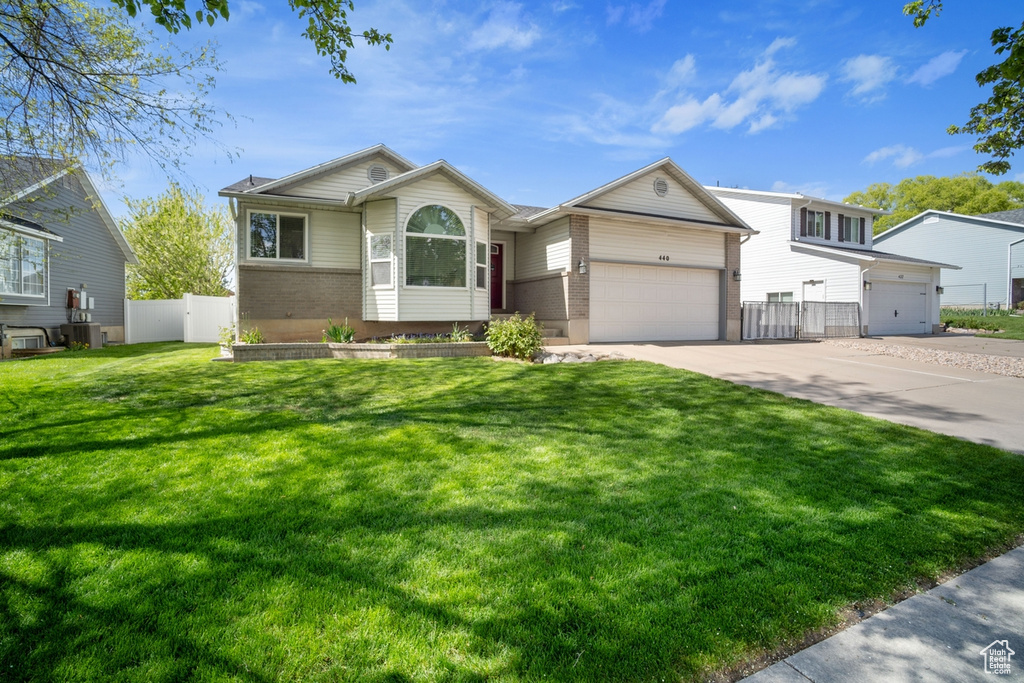 View of front of home with concrete driveway, an attached garage, fence, brick siding, and a front lawn