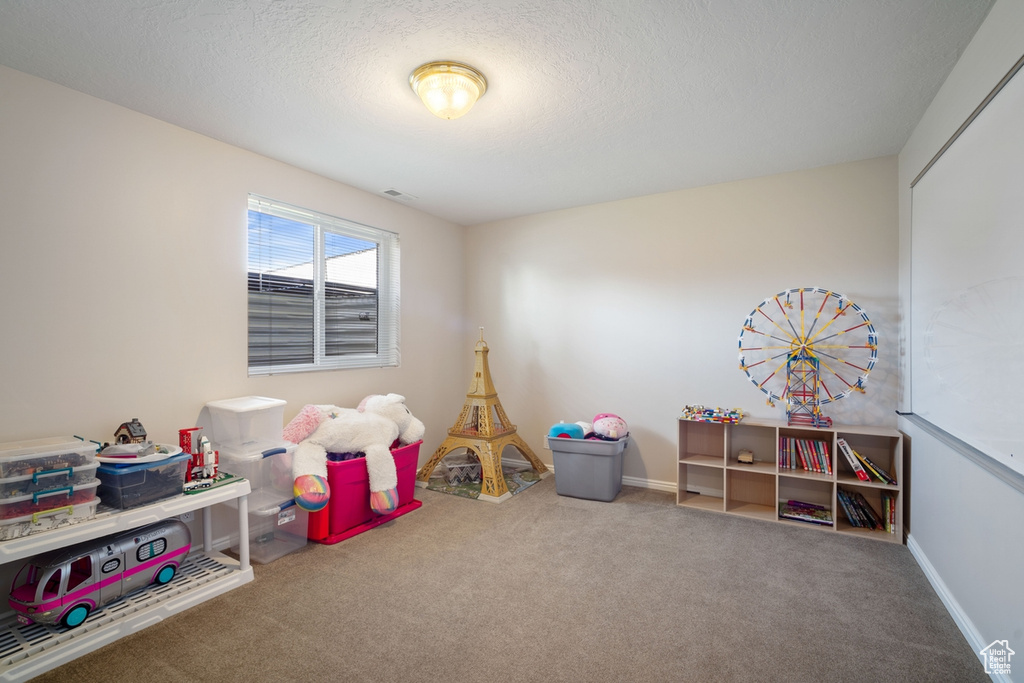 Recreation room featuring carpet, visible vents, baseboards, and a textured ceiling