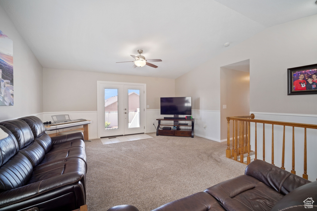 Carpeted living room featuring lofted ceiling, french doors, a ceiling fan, and a wainscoted wall