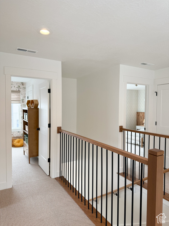 Hallway featuring visible vents, baseboards, carpet floors, and an upstairs landing