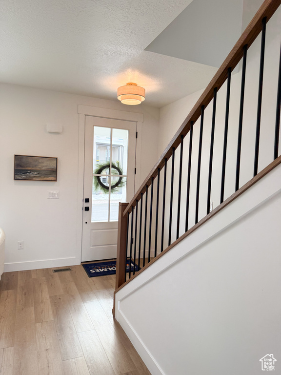 Foyer entrance featuring visible vents, wood finished floors, baseboards, stairway, and a textured ceiling