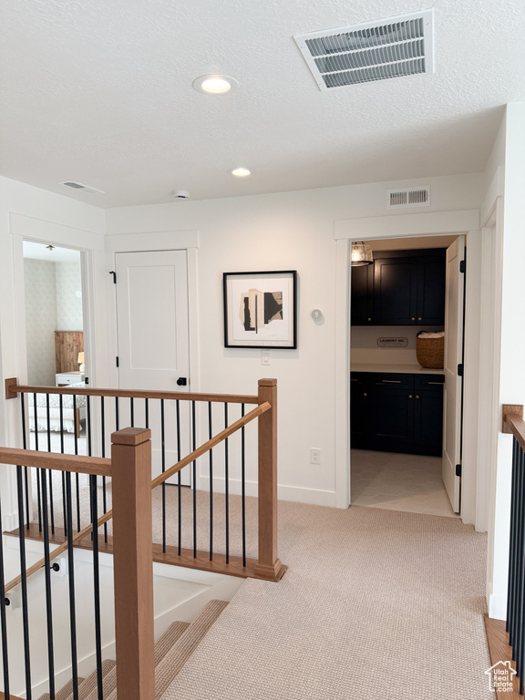 Hall featuring baseboards, visible vents, light carpet, and an upstairs landing