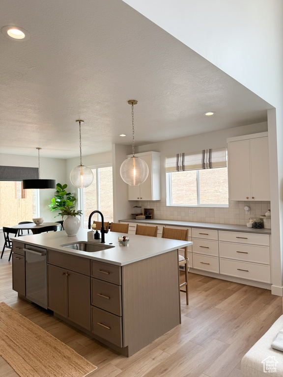 Kitchen featuring backsplash, stainless steel dishwasher, light wood-type flooring, a sink, and white cabinetry