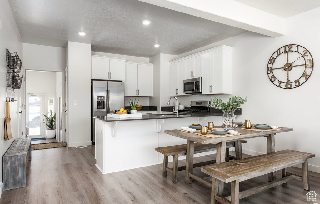 Kitchen featuring a peninsula, light wood-type flooring, white cabinetry, a sink, and appliances with stainless steel finishes