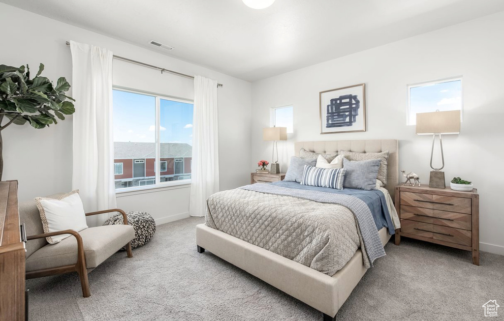 Bedroom with baseboards, light colored carpet, multiple windows, and visible vents