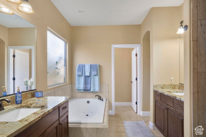 Full bath featuring a jetted tub, a sink, and two vanities