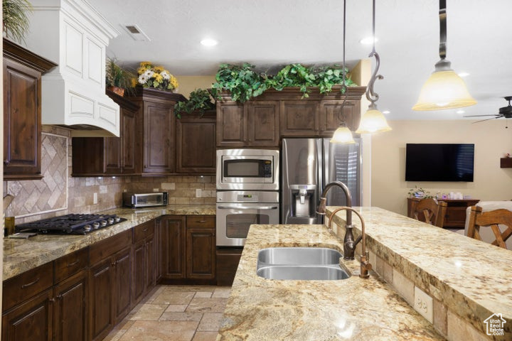 Kitchen with light stone counters, a sink, stainless steel appliances, a ceiling fan, and tasteful backsplash