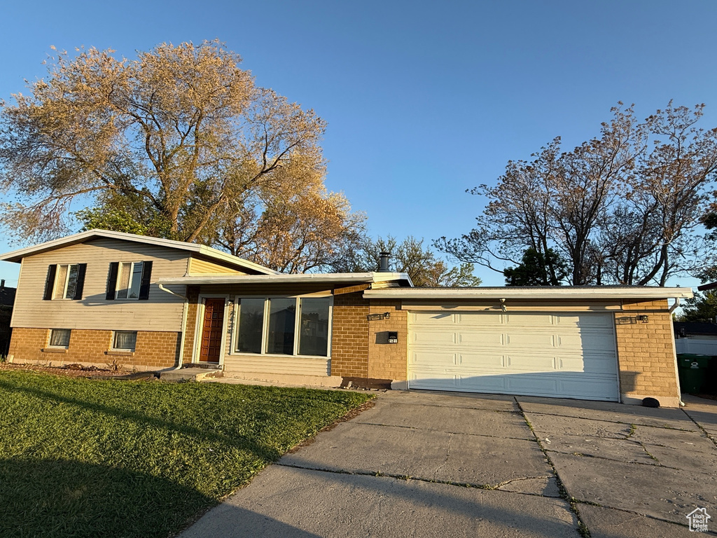 Tri-level home with brick siding, a garage, a front lawn, and concrete driveway
