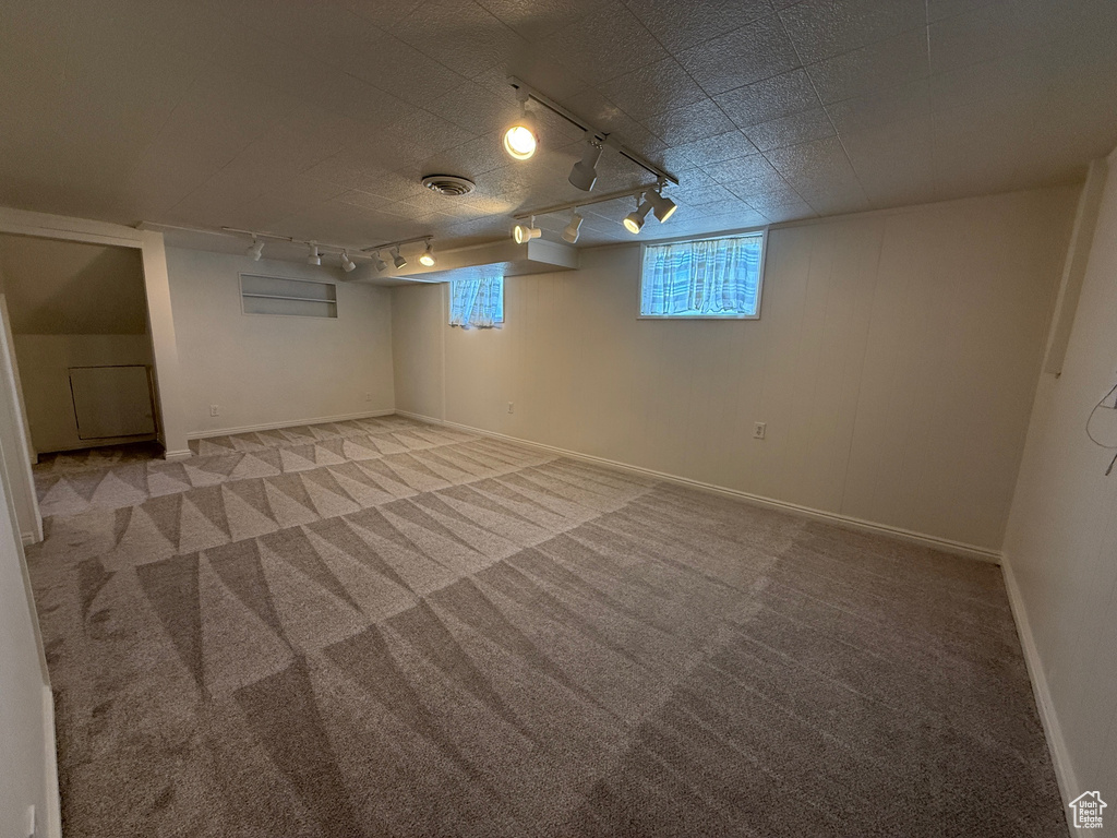 Basement featuring baseboards, light carpet, and rail lighting