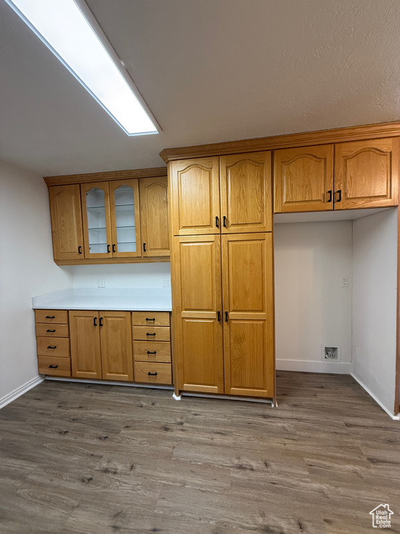 Kitchen featuring wood finished floors, glass insert cabinets, baseboards, light countertops, and brown cabinets