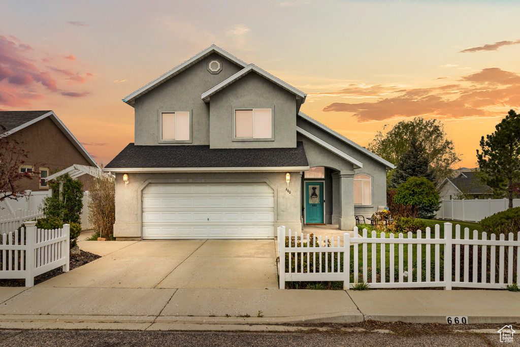 View of front facade with a garage, driveway, a fenced front yard, and stucco siding