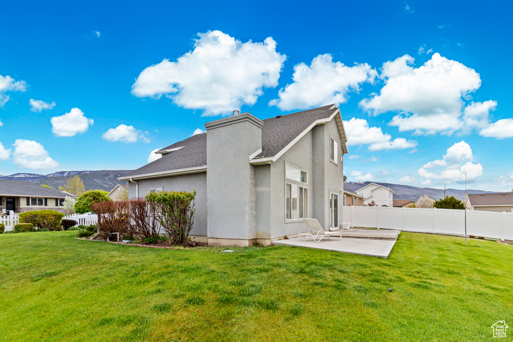View of home's exterior featuring fence, stucco siding, a patio area, a mountain view, and a yard