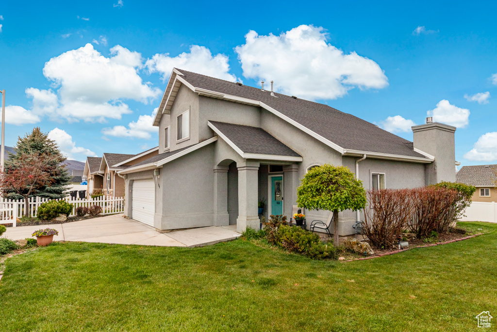 View of front of house with stucco siding, fence, driveway, and a front yard