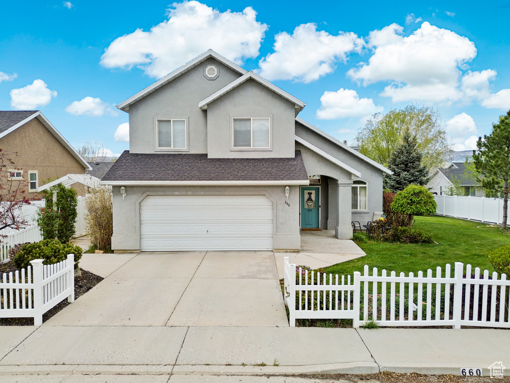 Traditional-style house with a garage, a front lawn, stucco siding, a fenced front yard, and driveway