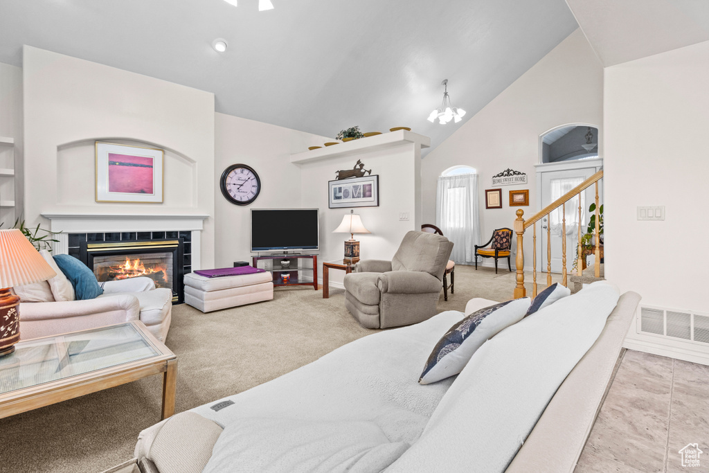 Carpeted living area featuring an inviting chandelier, arched walkways, high vaulted ceiling, a tiled fireplace, and visible vents