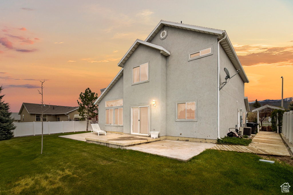 Back of house featuring central AC unit, a patio area, a fenced backyard, a yard, and stucco siding