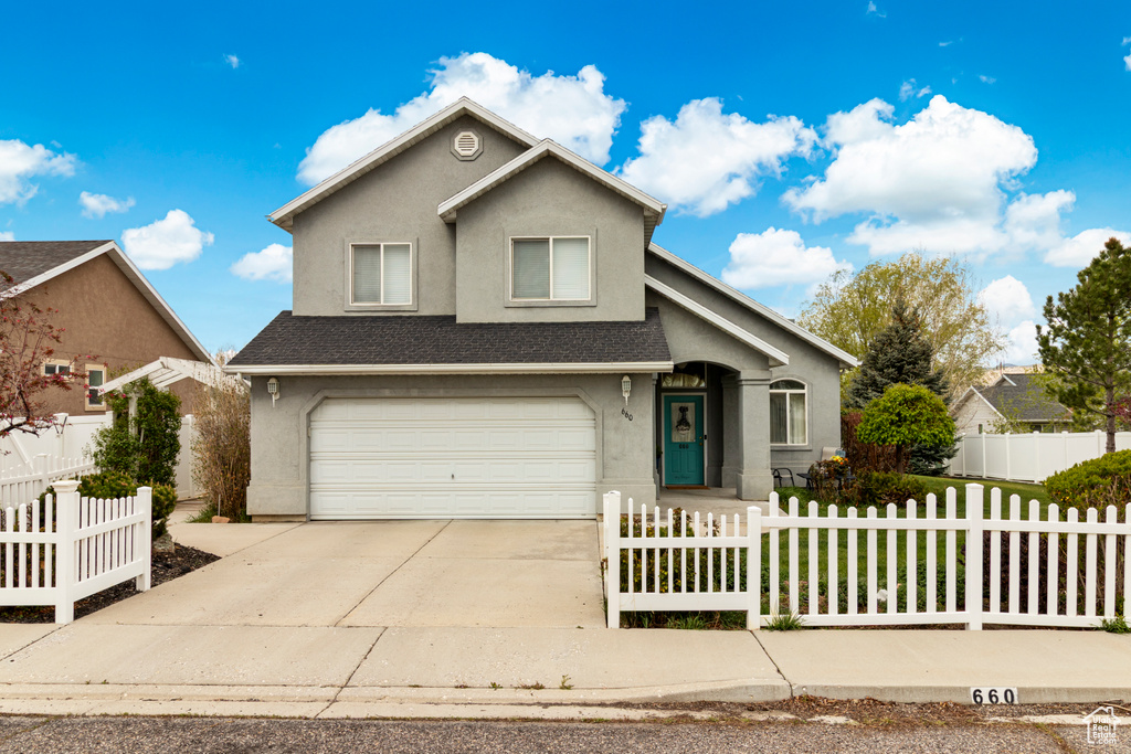 Traditional home with an attached garage, driveway, a fenced front yard, and stucco siding