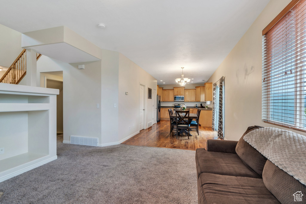 Carpeted living room with stairway, baseboards, an inviting chandelier, and visible vents
