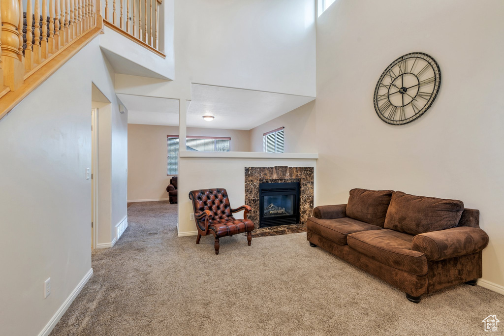 Carpeted living area featuring a high end fireplace, baseboards, stairs, and a towering ceiling