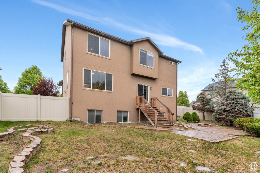 Rear view of property with stucco siding, a patio area, fence, and a yard