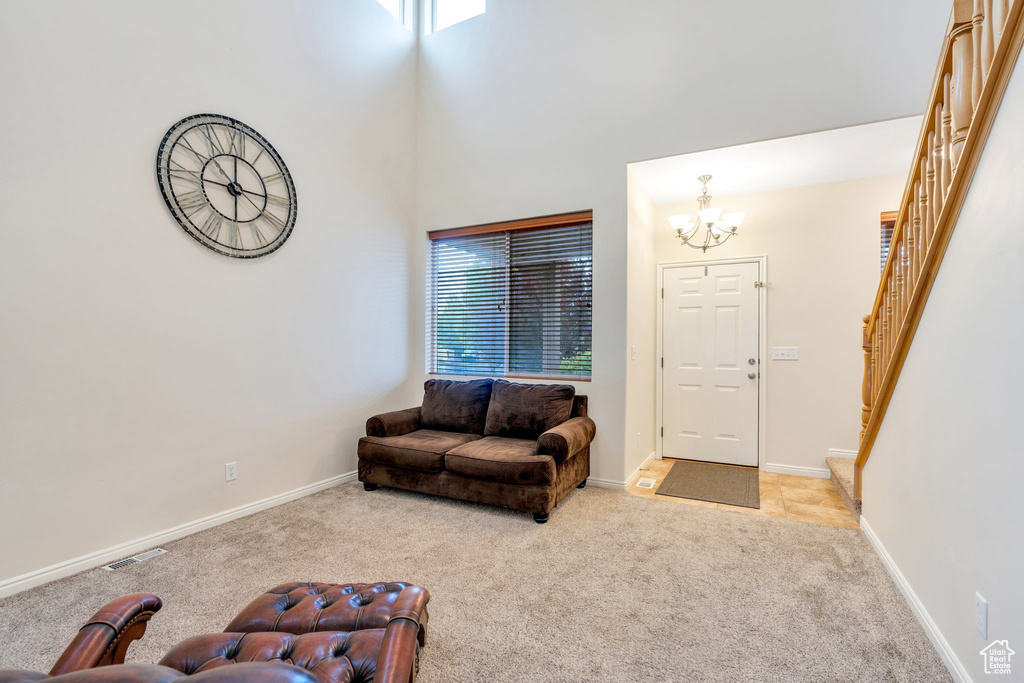 Living room featuring stairs, baseboards, a high ceiling, light colored carpet, and a notable chandelier