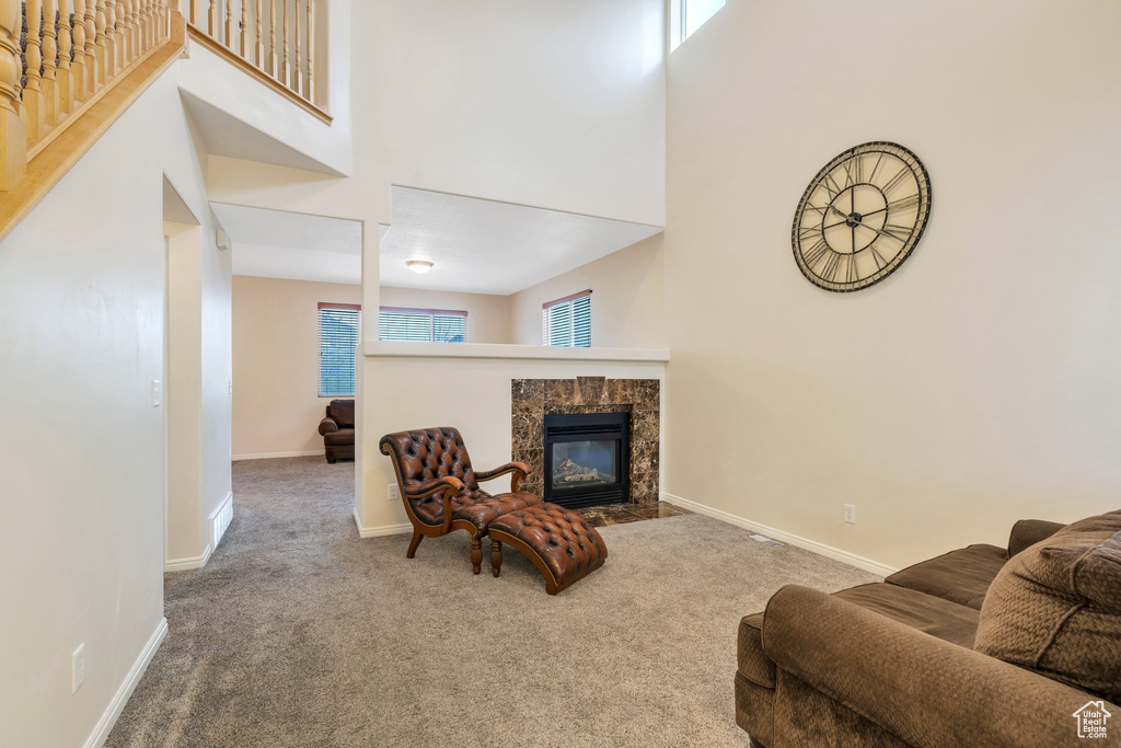 Carpeted living area featuring baseboards, a high ceiling, and a fireplace