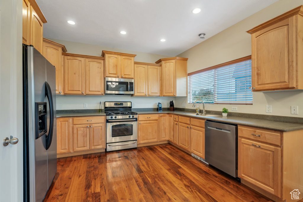 Kitchen with light brown cabinetry, dark countertops, a sink, stainless steel appliances, and dark wood-style floors