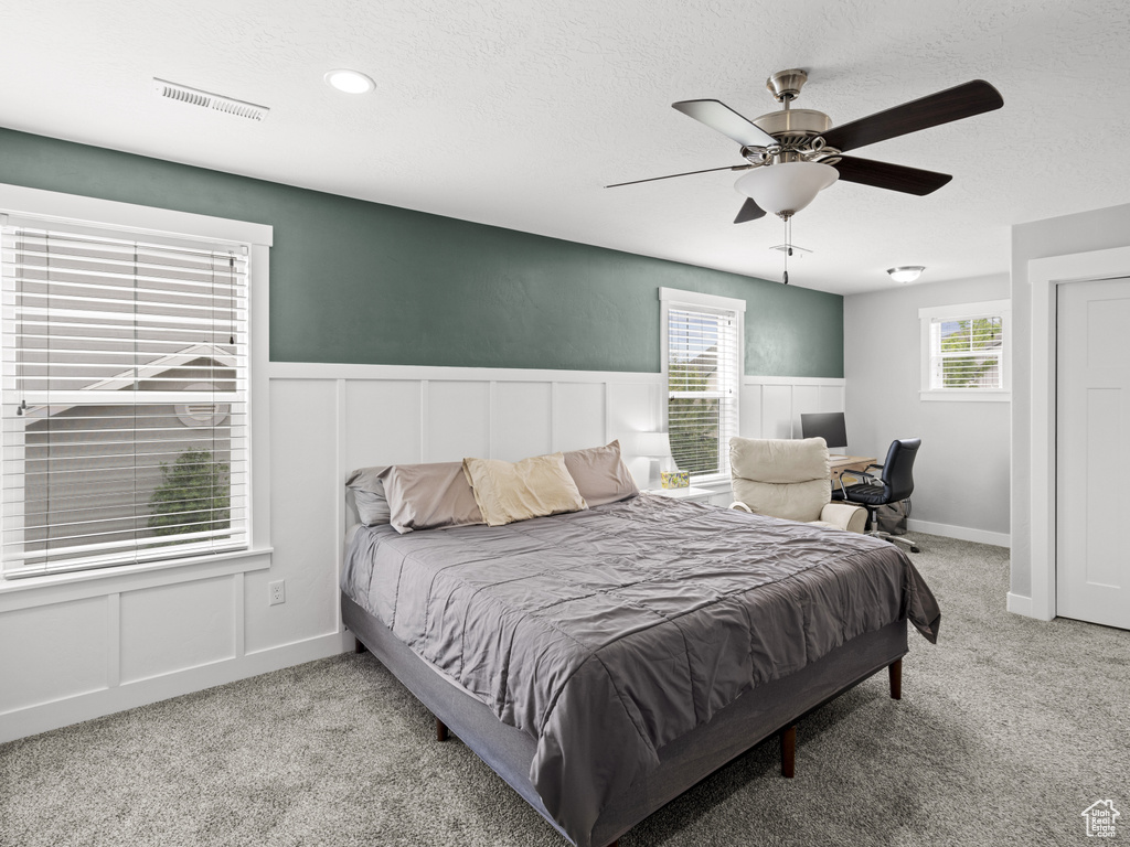 Carpeted bedroom featuring a wainscoted wall, a decorative wall, a textured ceiling, and visible vents