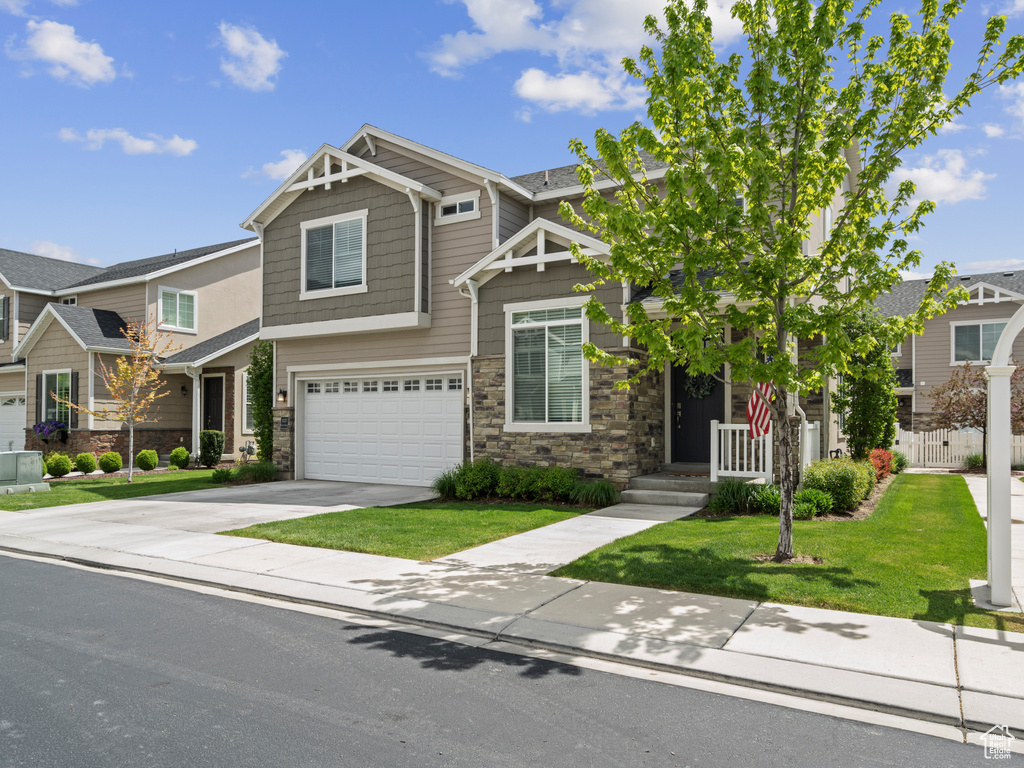 Craftsman house featuring a garage, fence, a front yard, stone siding, and concrete driveway