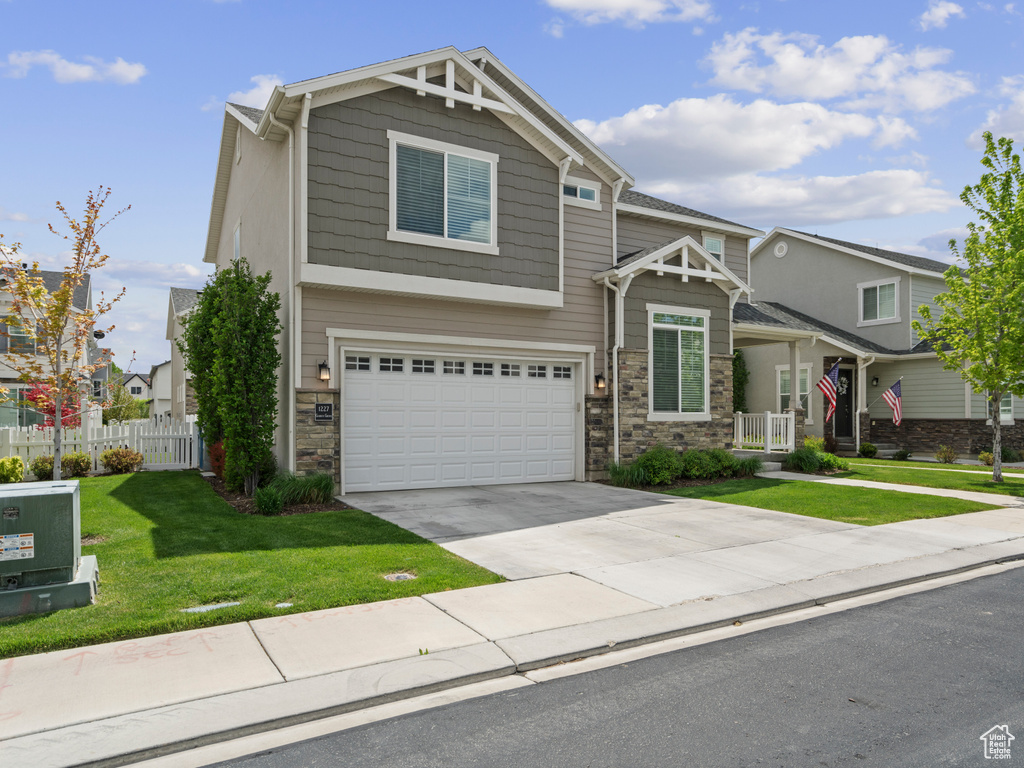 Craftsman inspired home featuring a garage, a front lawn, fence, and driveway