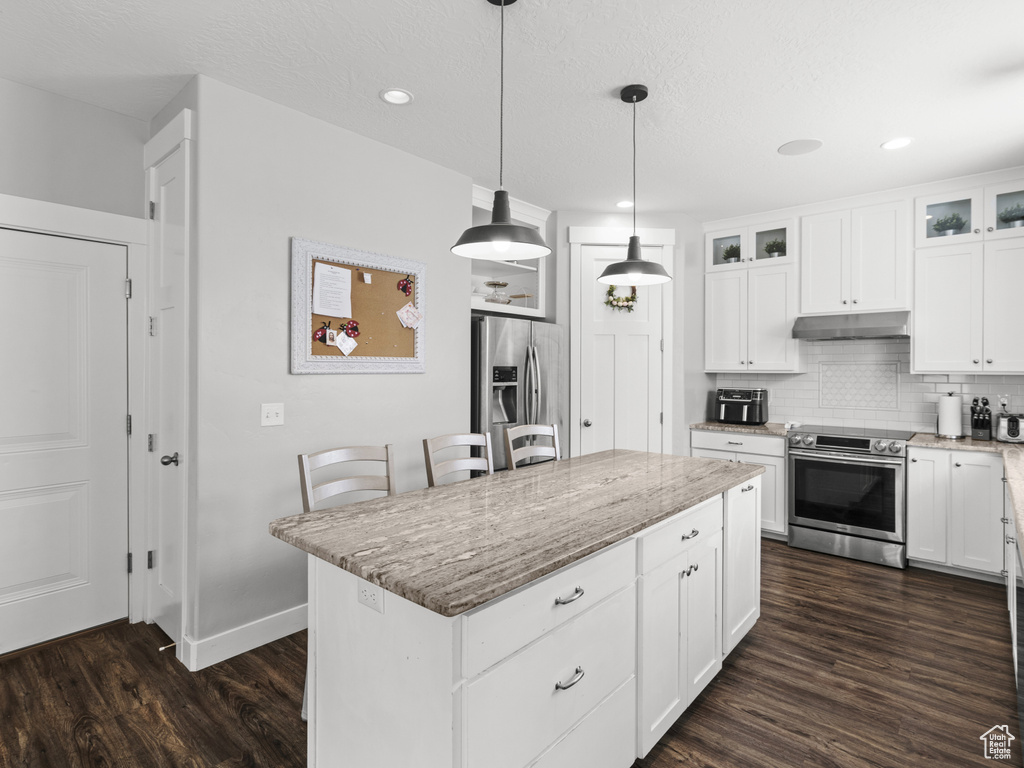 Kitchen with light stone countertops, dark wood-type flooring, under cabinet range hood, appliances with stainless steel finishes, and backsplash