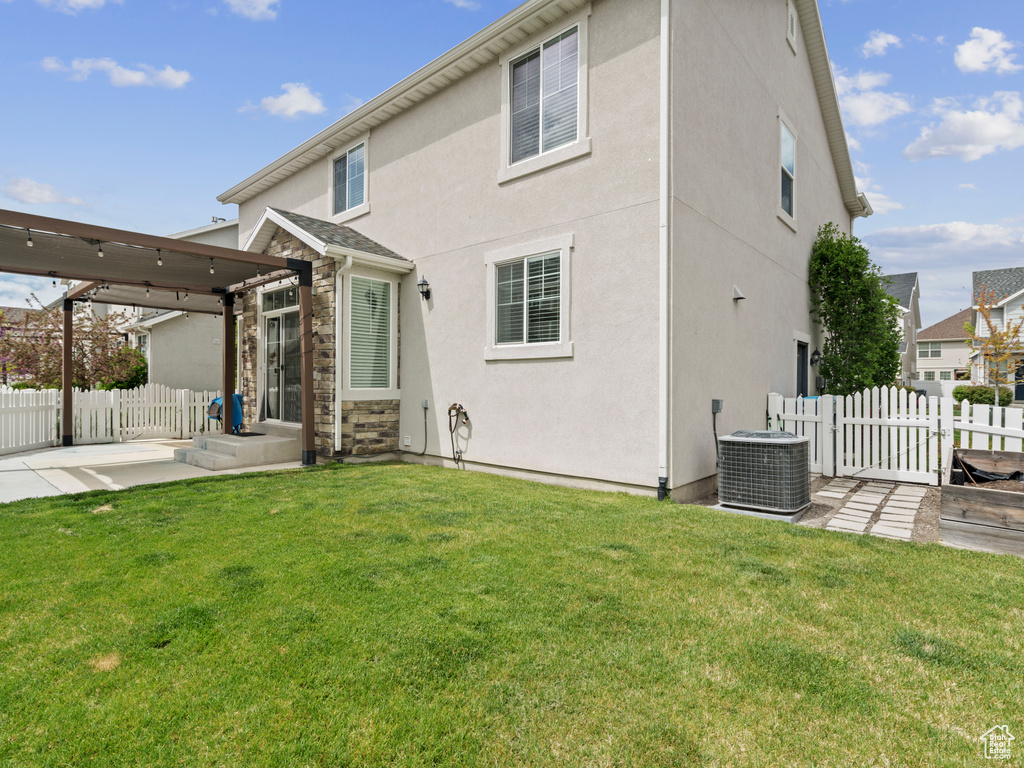 Rear view of property with stucco siding, central AC, a yard, and fence