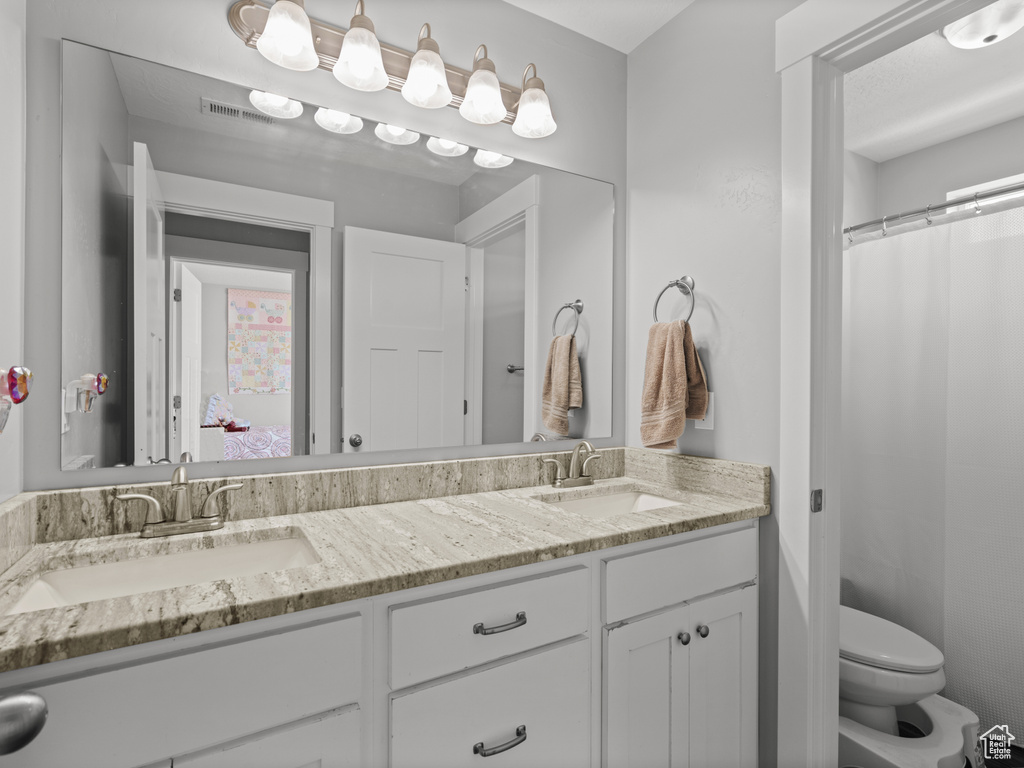 Bathroom with a sink, toilet, double vanity, and visible vents