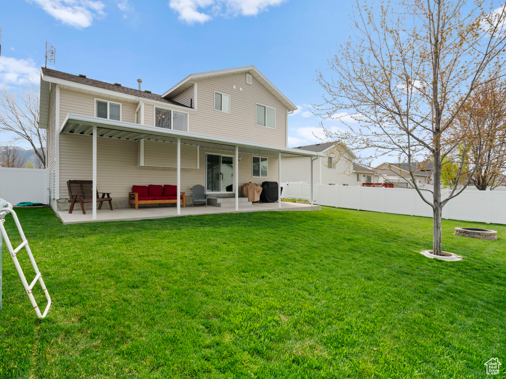 Rear view of house featuring a patio, a fenced backyard, and a lawn
