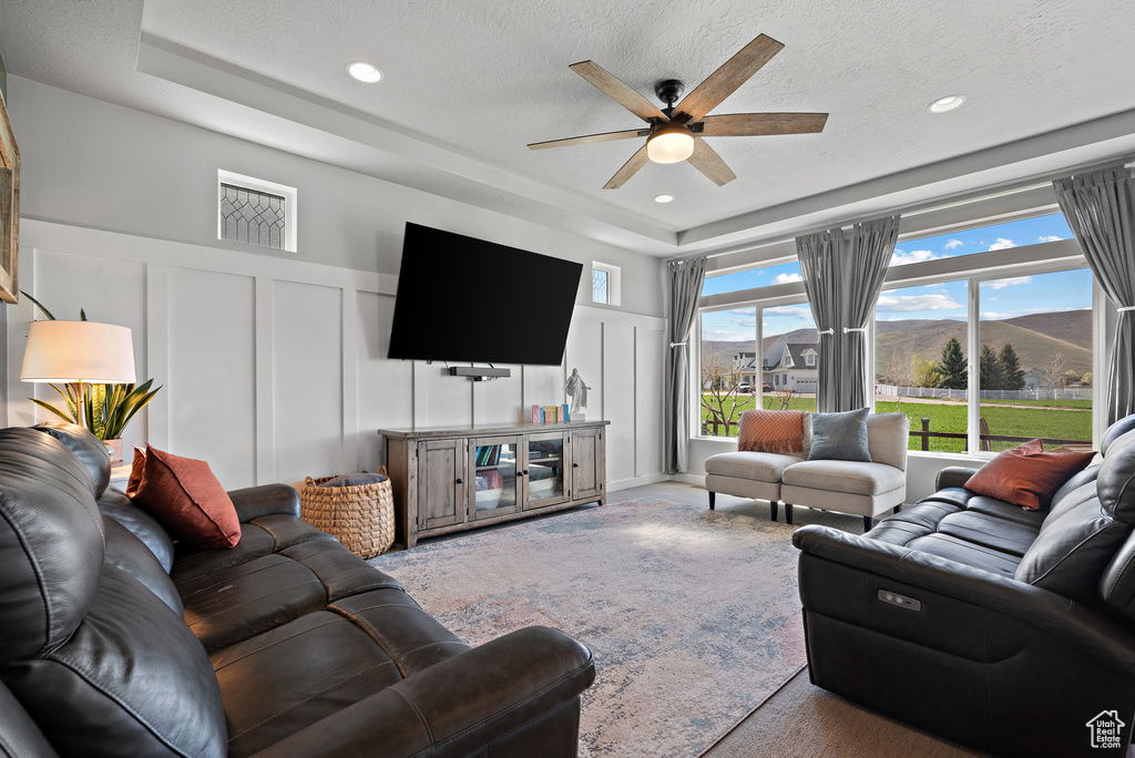 Living room featuring ceiling fan, a raised ceiling, carpet floors, a decorative wall, and recessed lighting
