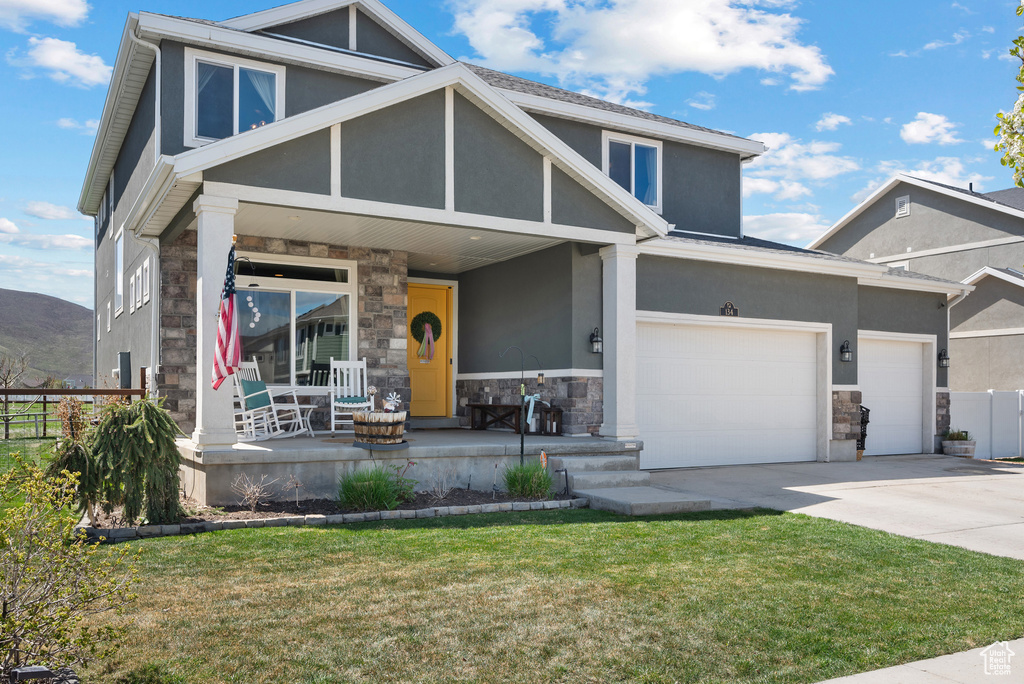 View of front facade featuring a porch, an attached garage, stone siding, and stucco siding