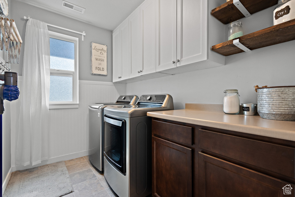 Laundry room with visible vents, cabinet space, a wainscoted wall, baseboards, and washer and clothes dryer