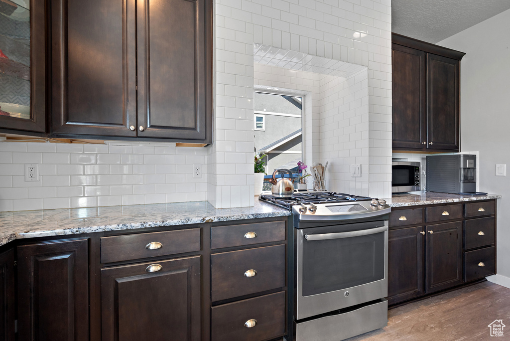 Kitchen with appliances with stainless steel finishes, wood finished floors, dark brown cabinets, and tasteful backsplash