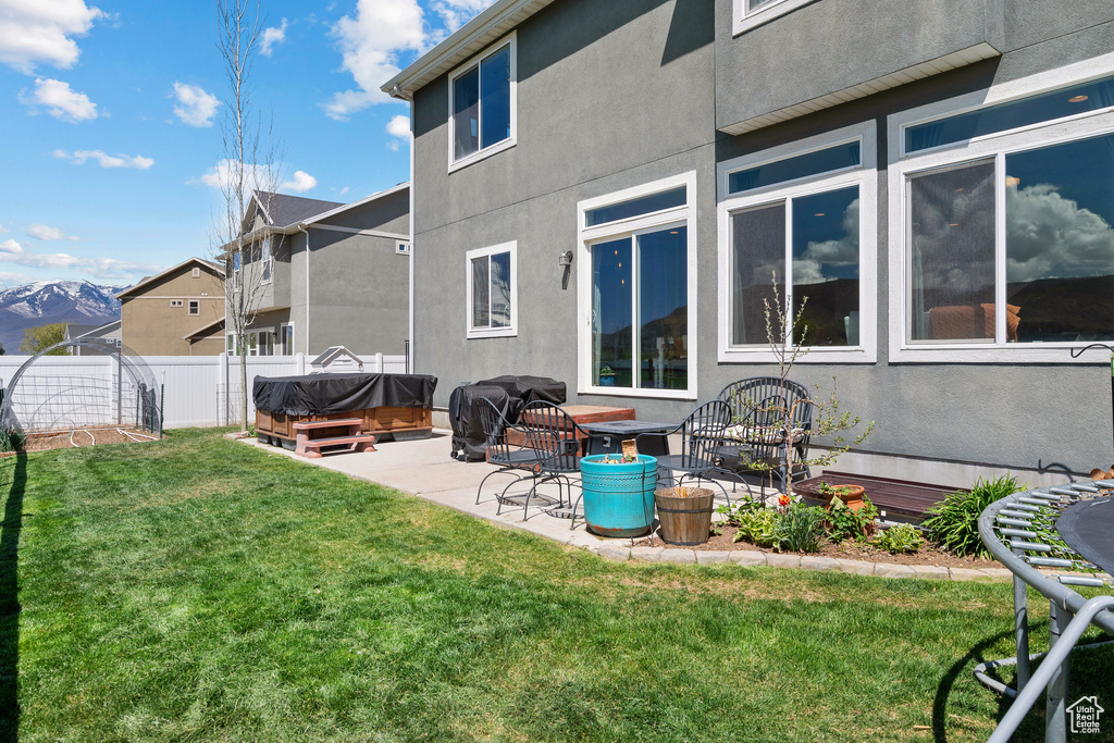 Rear view of house with a hot tub, a patio, fence, and stucco siding