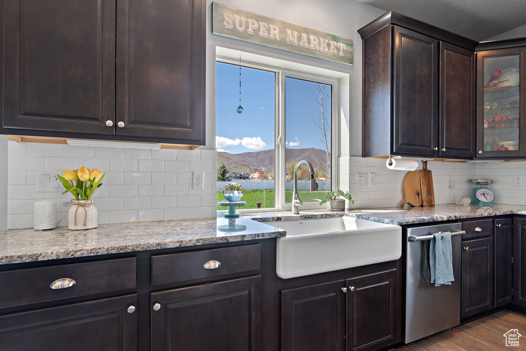 Kitchen featuring decorative backsplash, dark brown cabinetry, dishwasher, a sink, and glass insert cabinets