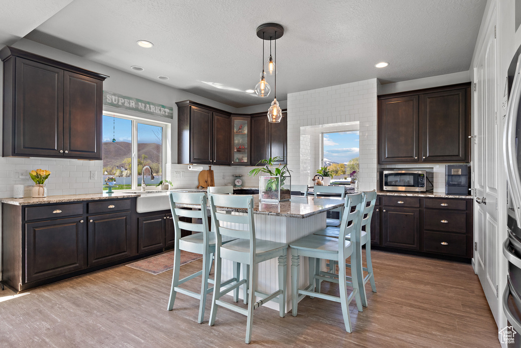 Kitchen featuring dark brown cabinets, light stone countertops, a kitchen breakfast bar, stainless steel microwave, and tasteful backsplash