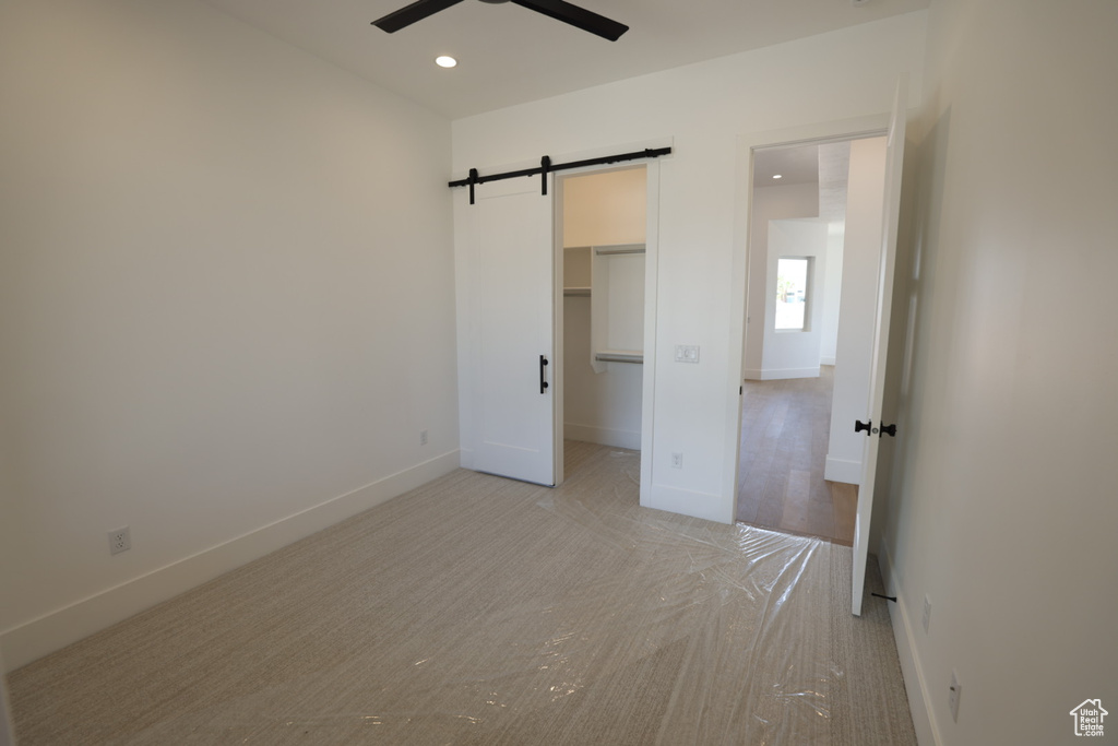 Unfurnished bedroom featuring light colored carpet, a barn door, a walk in closet, recessed lighting, and baseboards