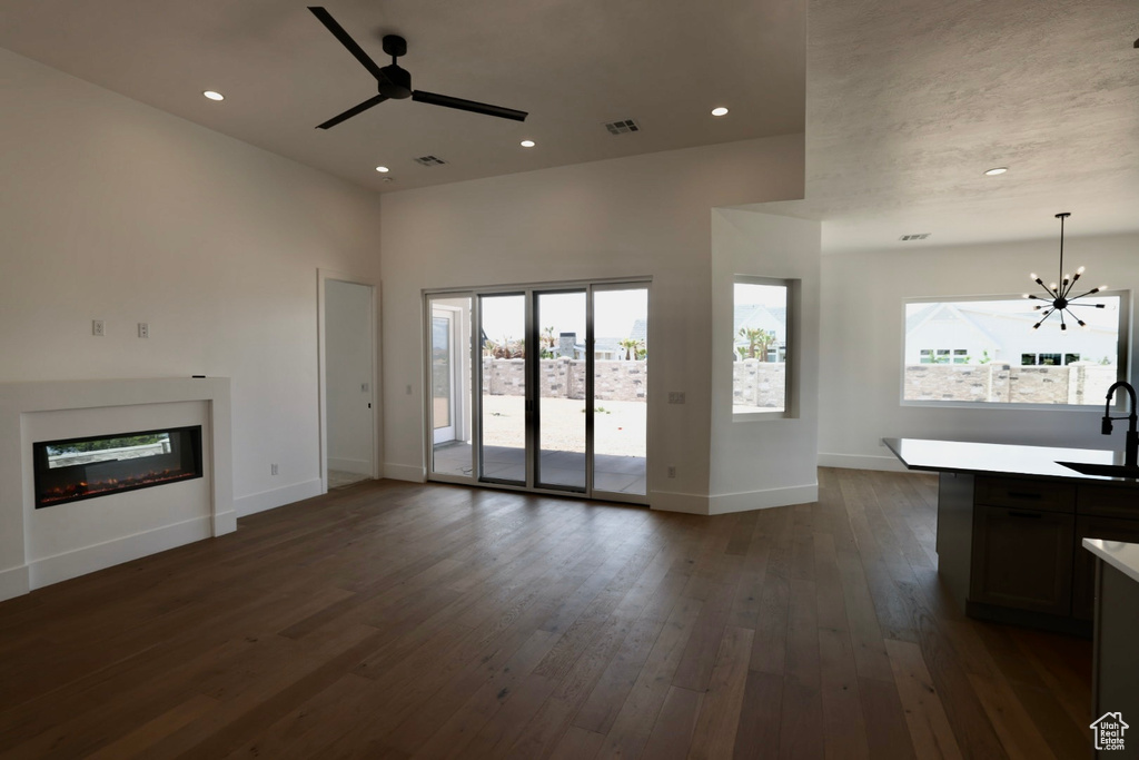 Unfurnished living room featuring visible vents, plenty of natural light, a sink, and ceiling fan with notable chandelier