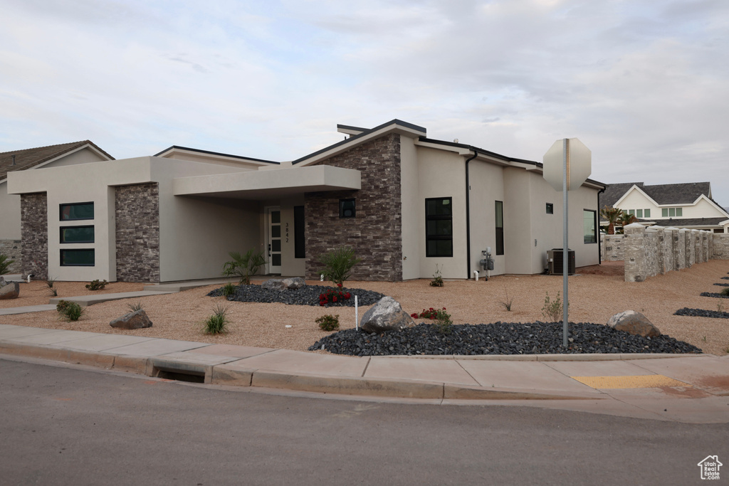 View of front of home with central air condition unit, stone siding, and stucco siding