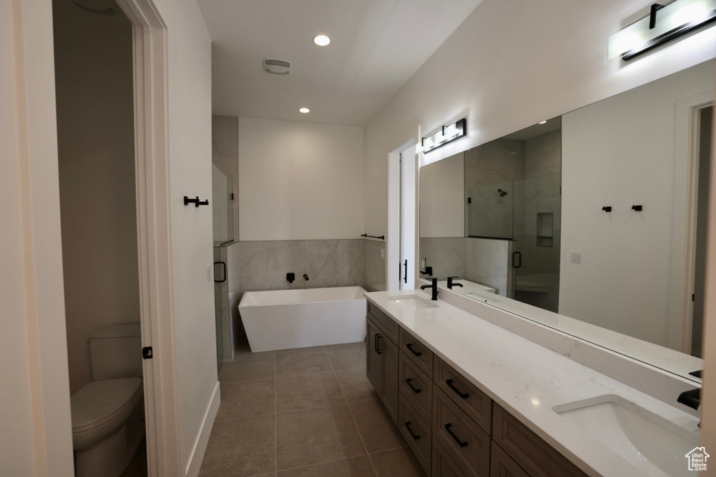 Bathroom featuring double vanity, a stall shower, a sink, tile patterned floors, and toilet