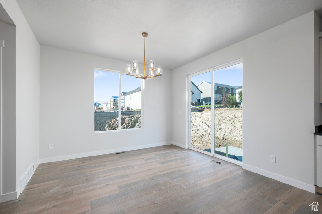 Unfurnished dining area featuring visible vents, baseboards, wood finished floors, and a notable chandelier